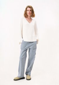 Witte, ribbelgebreide trui met V-hals, gecombineerd met blauw-wit gestreepte cargobroek en beige instappers. Gelaagd stof, relaxte pasvorm.
