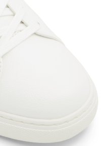 Valkoinen nahkakenkä, jossa on pyöreä kärki, koholleulottu pinta ja litteät puuvillan nauhat. Pohja on kumia, jossa on pystysuuntainen pito-kuvio.