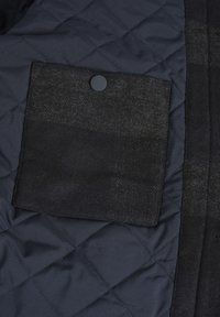 Tejido acolchado navy con un bolsillo de parche negro texturizado, que presenta un botón a presión negro circular. Acabado suave con materiales contrastantes.