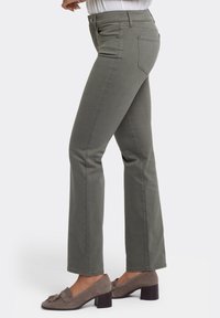 Pantalones acampanados de color verde oliva hechos de algodón suave, con una cintura de altura media, que cuentan con bolsillos delanteros y traseros, combinados con mocasines de tacón gris.