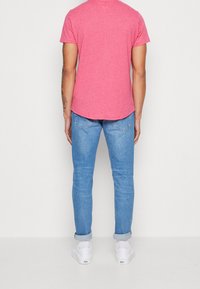 Red heathered t-shirt with a curved hem, paired with light blue jeans featuring rolled cuffs. White sneakers complete the outfit.