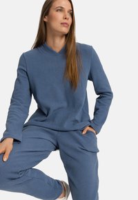 Completo da loungewear in morbido tessuto azzurro chiaro, con maniche lunghe, scollo a v e tasche. Presenta una vestibilità comoda e una texture delicata.