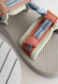 Sandal s šedou štruktúrovanou podrážkou, s viacfarebnými tkanými popruhmi v modrej, oranžovej a mentolovej farbe. Obsahuje ružový akcent na popruhu.