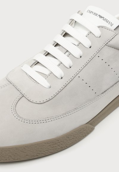 Baskets en daim gris clair avec lacets blancs et semelle en caoutchouc beige, avec le logo Emporio Armani sur la languette.