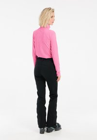 Prigludusi rožinė raibota ilgomis rankovėmis palaidinė, derinama su juodomis slidinėjimo kelnėmis, kurios turi užtrauktukus ties kulkšniais, dėvima su juodais slidinėjimo batais.