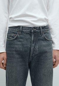 Jeans in denim scuro con taglio dritto, dotati di cinque tasche e cuciture a contrasto. Include chiusura con bottone e passanti per cintura.