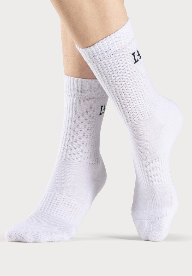 Calcetines de algodón blanco de caña corta con textura acanalada y detalle del logo "LA" en el puño, con puntas redondeadas y talón reforzado.