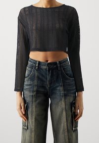 Black, cropped, long-sleeve sweater with a textured knit pattern. Paired with loose, faded blue denim cargo pants featuring side pockets.