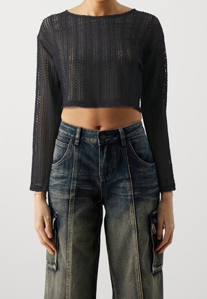 Zwart, korter gesneden, lange mouw trui met een textuur gebreid patroon. Gecombineerd met losse, vervaagde blauwe denim cargo broeken met zijzakken.