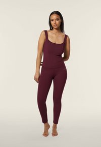 Completo di abbigliamento attivo in bordeaux, composto da un top aderente con spalline larghe e leggings a vita alta, realizzati in un materiale morbido e elastico.