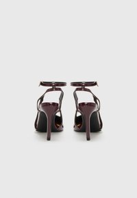 Burgundin patentoitu nahka korkeakorkoiset kengät, joissa on nilkkahihnat, leikattuja sivuja ja stiletto-korko. Hiukan pyöristetty varvasmuoto.