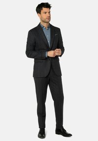 Dunkelgrauer Anzug mit dezentem Karomuster, kombiniert mit einem hellblauen Hemd. Der Anzug hat eine taillierte Passform und Revers mit Kerbe und wird durch schwarze Schuhe ergänzt.