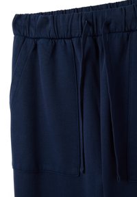 Navyblaue Sporthosen aus weichem Material, mit elastischem Bund, Kordelzügen und seitlichen Taschen. Glatte Textur mit gesteppten Nähten.