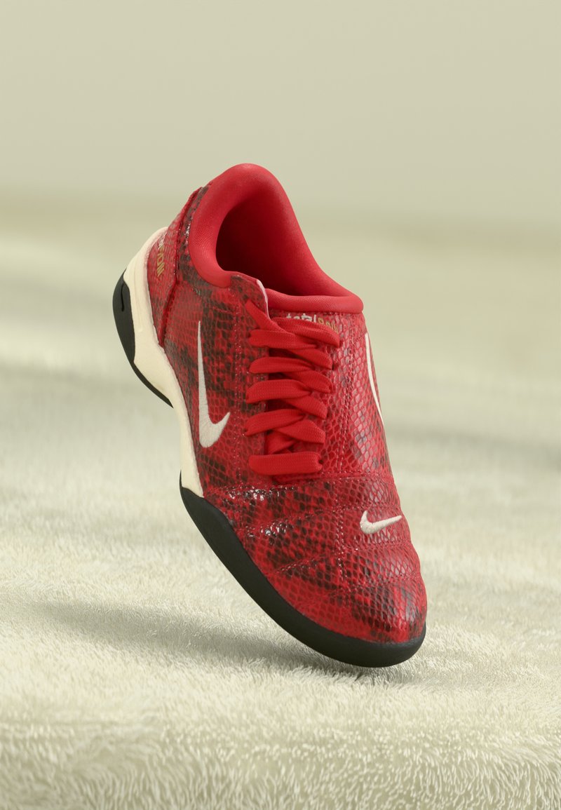 Sapatilhas Nike com padrão vermelho e preto, com atacadores vermelhos e logótipos swoosh brancos, sobre uma superfície texturizada bege.