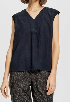 Ciemny, teksturowany top bez rękawów z dekoltem w serek i marszczonym detalem, zestawiony z luźnymi spodniami we wzory z geometrycznym motywem.