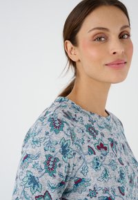 Top con estampado floral en suave material gris, que presenta coloridas flores turquesa y burdeos, con un escote redondo y una textura sutil.