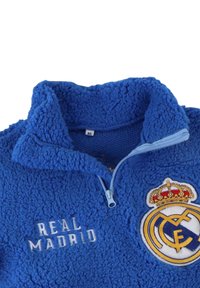 Pullover in pile blu con colletto alto, dotato di chiusura con zip. Include la scritta ricamata "Real Madrid" e il logo della squadra con una corona.