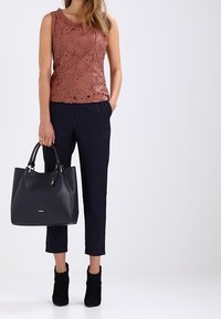 Spetstopp i dämpad rosé, kombinerad med navyblå rutiga cropped byxor. Svarta klackiga ankelskor och en strukturerad navyblå handväska.