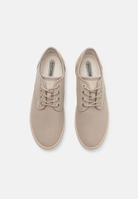 Beige lerretsko med runde tå, flate lisser, subtile sømdetaljer, gummisåler og teksturert stoff.