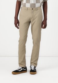 Beige bomullbyxor med slim fit, med en traditionell dragkedja och knappstängning, sidofickor och diskreta sömnadsdetaljer.