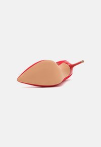 Chaussure à talon aiguille rouge avec un bout pointu, dessus en tissu et semelle lisse beige avec des nervures subtiles pour une meilleure adhérence.