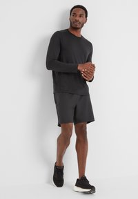Black long-sleeve athletic shirt paired with black shorts, showcasing a smooth texture and a simple design, worn with dark athletic shoes.