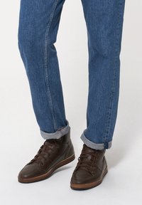 Brązowe skórzane sneakersy typu high-top z fakturowanym wykończeniem, ciemnymi sznurowadłami i gumowymi podeszwami, połączone z zwężającymi się dżinsami.