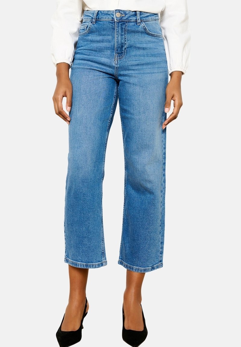 Högmidjade blå denimjeans med rak benklippning, med fram- och bakfickor samt en ren fåll. Bärs med svarta klackar.