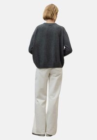Dunkelgrauer oversized Pullover mit rundem Ausschnitt, kombiniert mit weißen weit geschnittenen Hosen. Die Stoffe wirken weich mit einer glatten Textur.