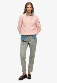 Jasnoróżowy sweter w warkocze nałożony na dżinsową koszulę, w połączeniu z prążkowanymi spodniami i ciemnymi loafersami. Prosty design o luźnym kroju.