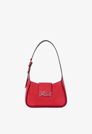Piros bőr kézitáska ívelt sziluettel, cipzáras fedéllel és ezüst színű logó díszítéssel. Állítható pánt díszes fémalkatrészekkel.