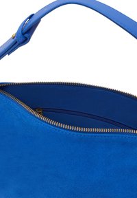 Blå mockaväska med dragkedjeslutning, med ett slätt läderhandtag och en kontrasterande inredning. Dragkedjan har en guldtonad finish.