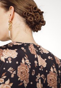 Abito floreale nero con grandi rose pesche e piccoli fiori bianchi. Orecchini a catena dorati con un accento di perla. Capelli acconciati in uno chignon texture.