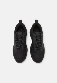 Scarpe da ginnastica nere caratterizzate da una combinazione di materiali lisci e testurizzati, design con lacci, imbottitura e marchio del produttore sulla linguetta.