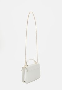 Kleine rechteckige weiße Handtasche mit oberem Griff und langem goldenen Kettenriemen vor schlichter weißer Hintergrund.