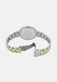 Hõbe- ja kullatooniga roostevabast terasest kell, millel on ümar korpus, poleeritud viimistlus ja turvaline pandla. Omab minimalistlikku disaini koos graveeritud üksikasjadega.