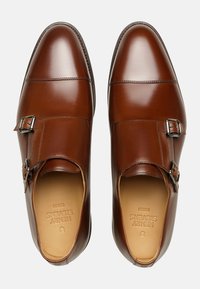 Chaussures double boucle en cuir marron avec une finition brillante, bout rond et boucles en métal argenté. Texture lisse et design minimaliste.