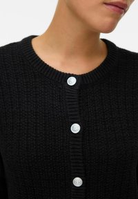 Black knitted cardigan featuring a round neckline, textured fabric, and six silver buttons down the front with embossed design details.