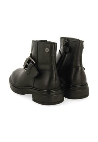 Botas de cuero negras hasta el tobillo con un acabado texturizado, que presentan una cremallera lateral y un detalle de hebilla, tacón bajo y grueso, y punta redonda.