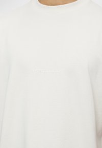 Bílé tričko vyrobené z měkké bavlny s kulatým výstřihem a krátkými rukávy. Na přední straně se nachází vyražené logo "PEGADOR".