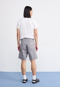 Pantalones cortos de carga grises con múltiples bolsillos, hechos de un tejido duradero. Combinados con una camiseta blanca lisa y sandalias negras con calcetines blancos.