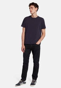 T-shirt di cotone blu navy con scollatura rotonda, abbinata a jeans neri slim-fit. Il modello indossa sneaker grigie con strisce bianche.