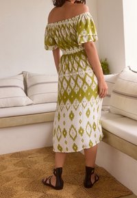 Robe verte et blanche à épaules dénudées avec un motif géométrique, taille élastique et manches courtes. Stylisée avec des sandales noires.