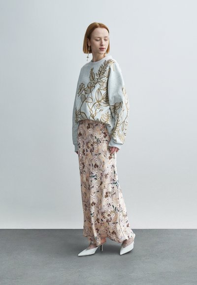 Γκρι φούτερ με χρυσή κεντητή διακόσμηση λουλουδιών, συνδυασμένο με μια μακριά φούστα σε απαλούς παστέλ τόνους με λουλουδένιο μοτίβο. Το λευκό μυτερό τακούνι ολοκληρώνει την εμφάνιση.