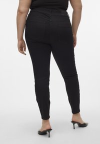 Svarta denim skinny jeans med medelhög midja, bakfickor och en slät textur. Bärs med svarta klackslippers.