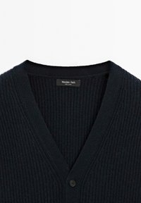 Svart ribbat stickat kardigan med V-ringning, en synlig knapp och "Massimo Dutti"-etikett inuti kragen.