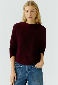 Bordeaux gebreide trui met een ronde hals, verlaagde schouders en ribgebreide manchetten, gecombineerd met blauwe denim broek met voorzakken.