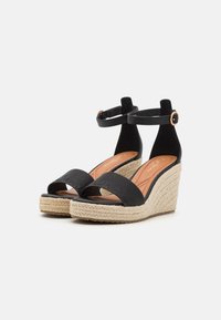 Sorte svarte kilehæler med en vevd jute såle, med ankelreim og front slipper-design. Glatt finish med teksturert remdetalj.