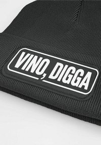 Black ribbed beanie featuring a rectangular white patch with the text "VINO, DIGGA" in bold black letters. Simple design, textured fabric.