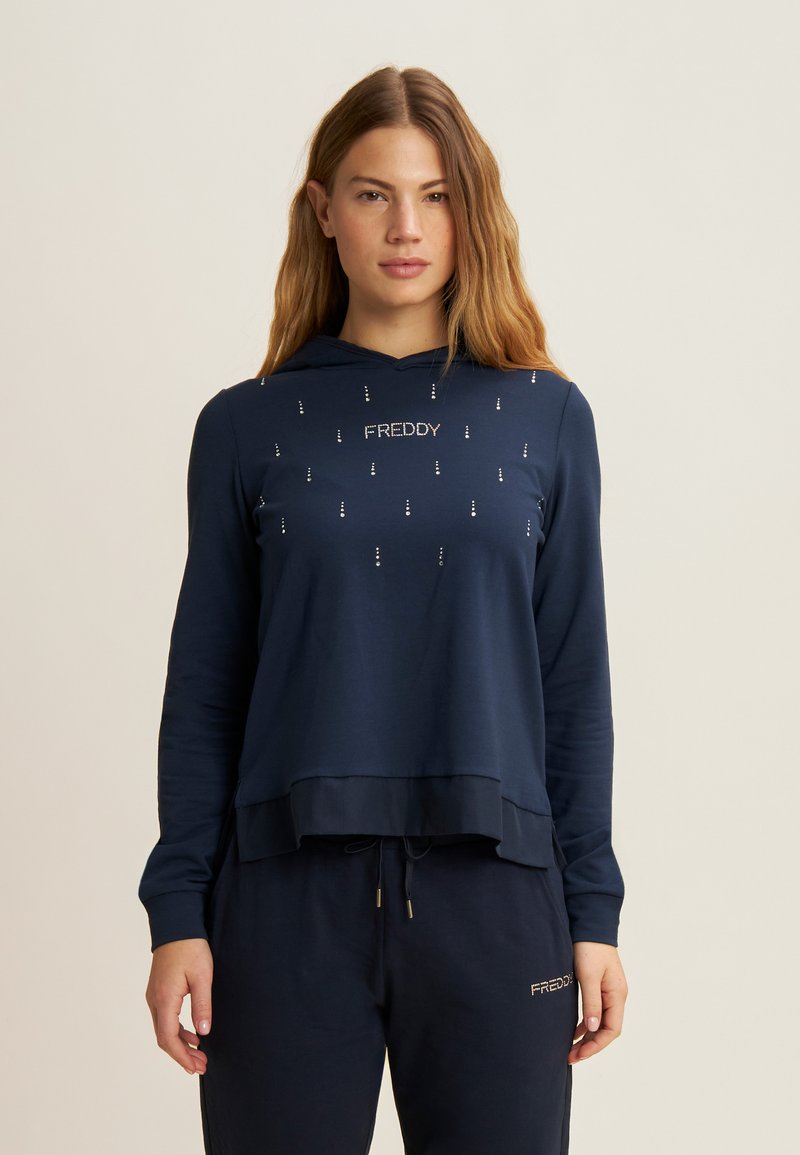 Felpa blu navy con vestibilità ampia, caratterizzata da un logo frontale e borchie decorative. Tessuto morbido, maniche lunghe e dettaglio con cordoncino all'orlo.